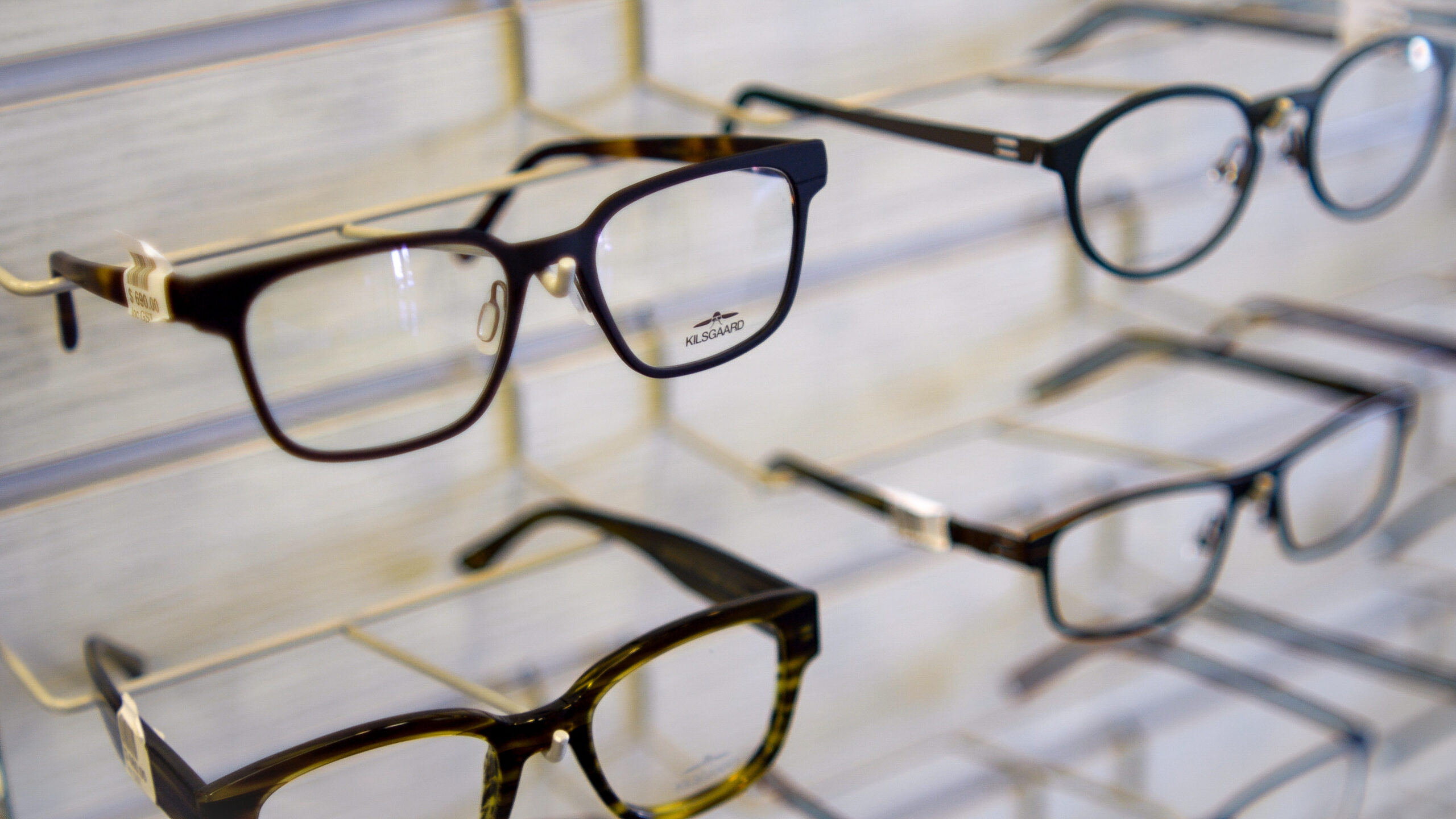 Close-up of black rectangular eyeglass frames on a display rack; Kilsgaard brand visible on the lens area