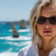 bill bass Woman wearing black sunglasses and a white shirt standing by a bright blue ocean backdrop.