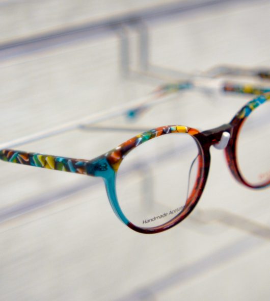 Close-up of colorful patterned eyeglasses on a display shelf in a bright store environment.